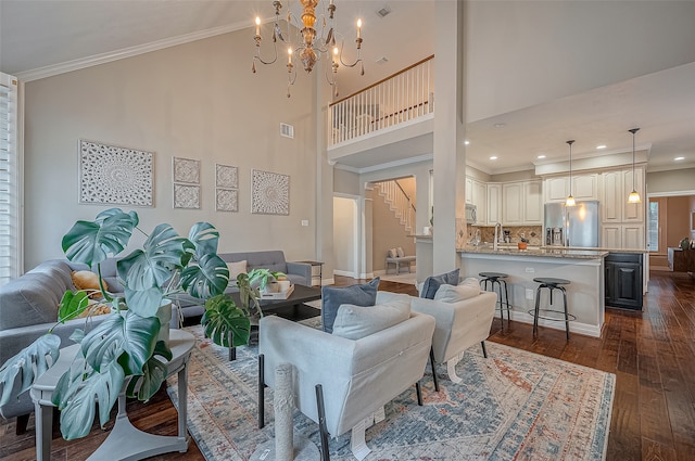 living room with a towering ceiling, sink, dark hardwood / wood-style flooring, ornamental molding, and an inviting chandelier