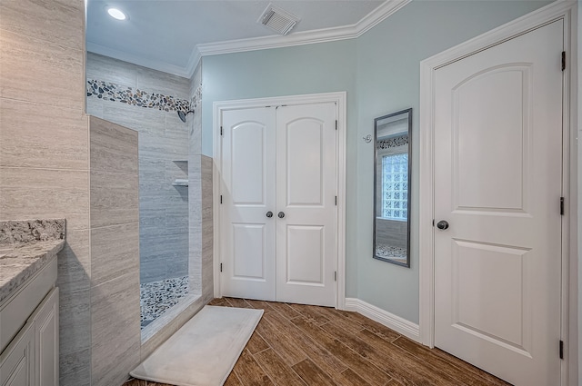 bathroom with wood-type flooring, vanity, crown molding, tile walls, and a tile shower