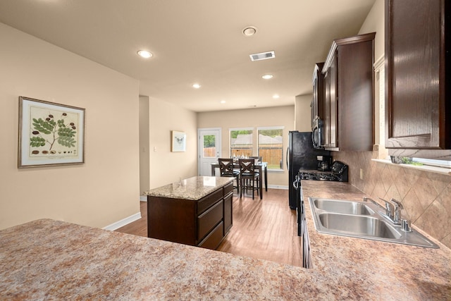 kitchen with a kitchen island, light hardwood / wood-style flooring, stainless steel appliances, sink, and tasteful backsplash