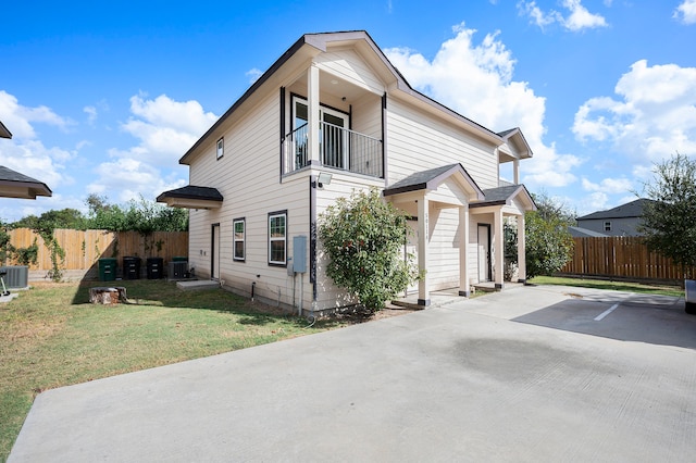 view of front of house featuring central AC, a balcony, and a front lawn