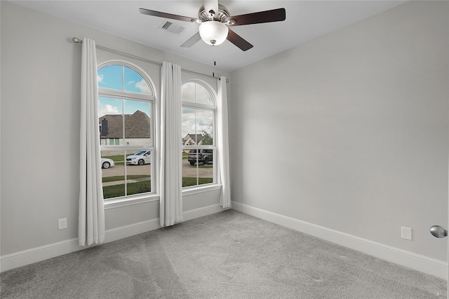 spare room featuring light carpet, ceiling fan, and a wealth of natural light