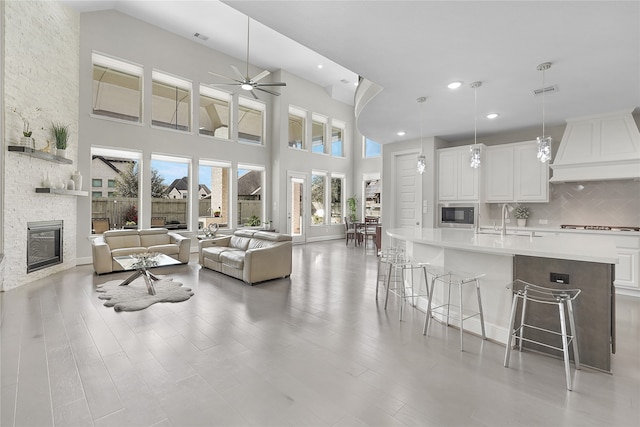 living room with ceiling fan, light hardwood / wood-style flooring, a fireplace, a towering ceiling, and sink