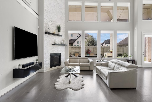 living room featuring dark wood-type flooring, a stone fireplace, and a towering ceiling