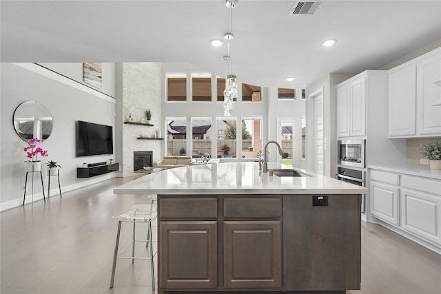 kitchen with an island with sink, dark brown cabinets, stainless steel appliances, sink, and white cabinetry