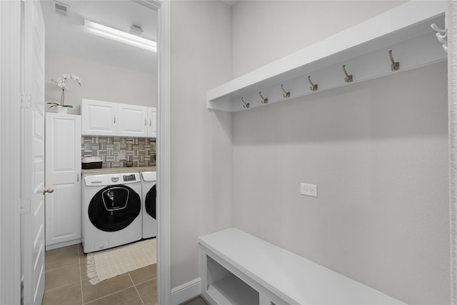 clothes washing area with washing machine and dryer, cabinets, and dark tile patterned floors