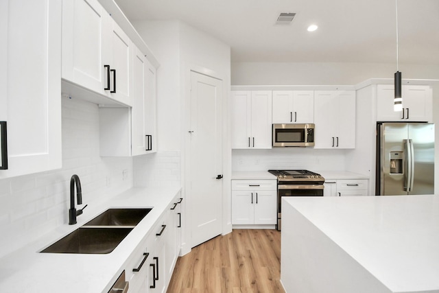 kitchen with white cabinetry, sink, stainless steel appliances, light hardwood / wood-style flooring, and decorative light fixtures