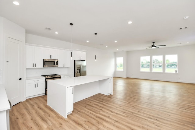 kitchen with a center island, white cabinets, hanging light fixtures, light hardwood / wood-style floors, and stainless steel appliances