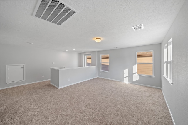 carpeted empty room with a textured ceiling and a wealth of natural light