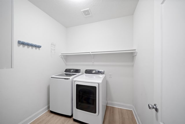 clothes washing area featuring light hardwood / wood-style flooring, a textured ceiling, and independent washer and dryer