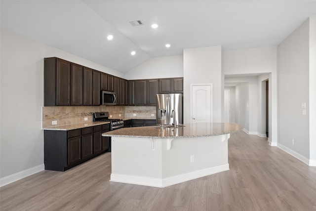 kitchen with a center island with sink, sink, vaulted ceiling, appliances with stainless steel finishes, and a kitchen bar