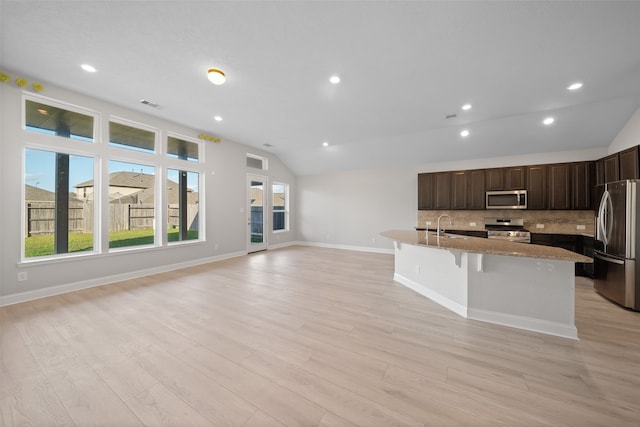 kitchen featuring sink, light hardwood / wood-style floors, lofted ceiling, a kitchen island with sink, and appliances with stainless steel finishes