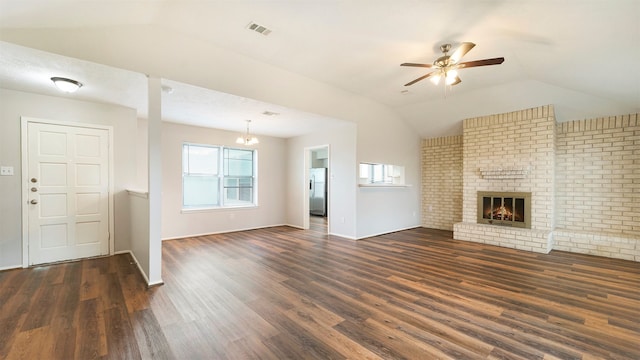 unfurnished living room with lofted ceiling, a brick fireplace, dark wood-type flooring, ceiling fan with notable chandelier, and brick wall