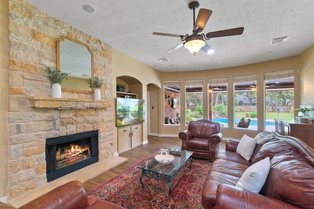 living room with hardwood / wood-style floors, a textured ceiling, a stone fireplace, and ceiling fan