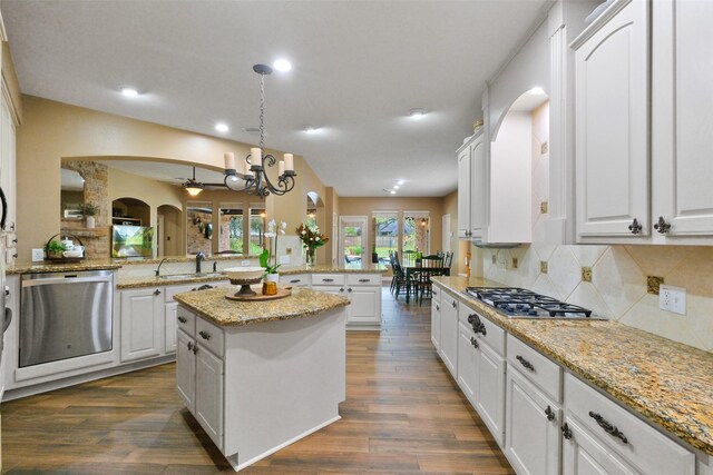 kitchen featuring appliances with stainless steel finishes, a kitchen island, decorative light fixtures, dark hardwood / wood-style floors, and white cabinetry