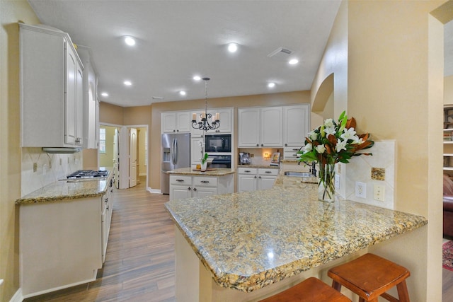 kitchen with kitchen peninsula, appliances with stainless steel finishes, light wood-type flooring, light stone countertops, and white cabinets