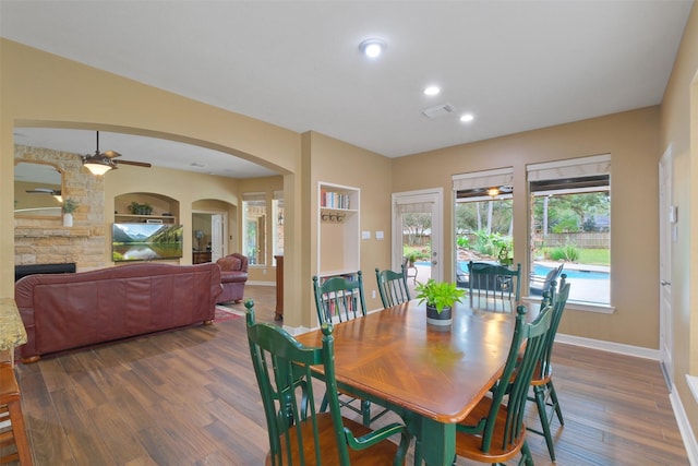 dining room with ceiling fan, a fireplace, and dark wood-type flooring