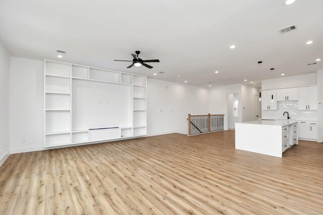 unfurnished living room with ceiling fan, sink, and light wood-type flooring