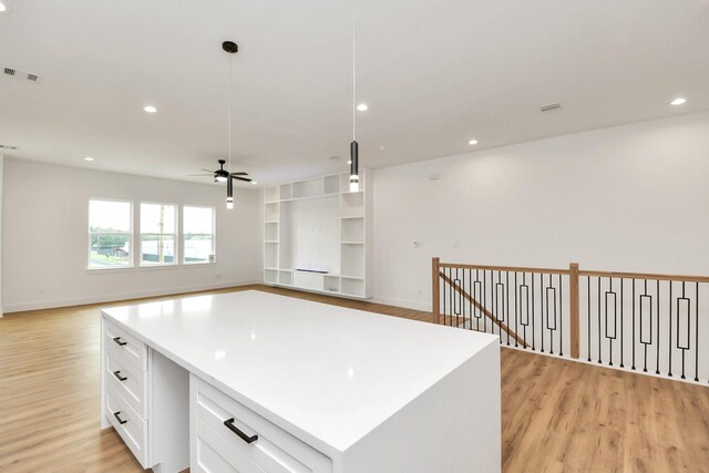 kitchen with light wood-type flooring, ceiling fan, decorative light fixtures, white cabinets, and a center island