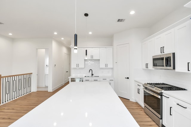 kitchen with white cabinetry, hanging light fixtures, light wood-type flooring, and appliances with stainless steel finishes