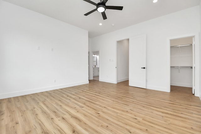 unfurnished bedroom with a spacious closet, ceiling fan, light wood-type flooring, and a closet