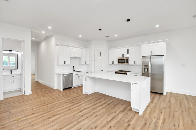 kitchen with pendant lighting, light hardwood / wood-style floors, appliances with stainless steel finishes, a kitchen island, and white cabinetry