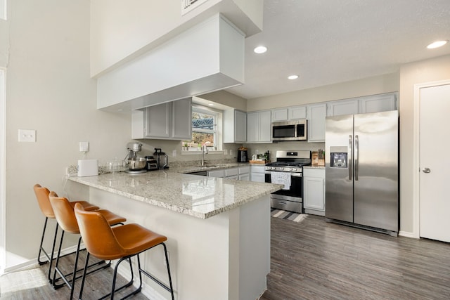 kitchen featuring kitchen peninsula, appliances with stainless steel finishes, a kitchen bar, and dark hardwood / wood-style floors