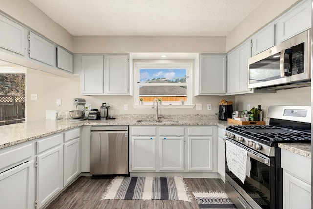 kitchen with appliances with stainless steel finishes, sink, white cabinets, dark wood-type flooring, and light stone counters