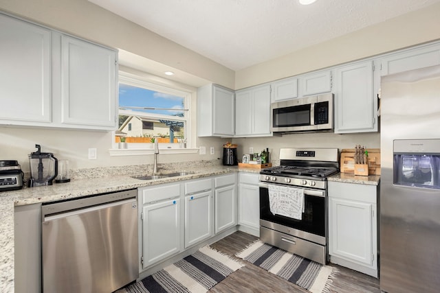 kitchen with white cabinetry, light stone counters, stainless steel appliances, and sink