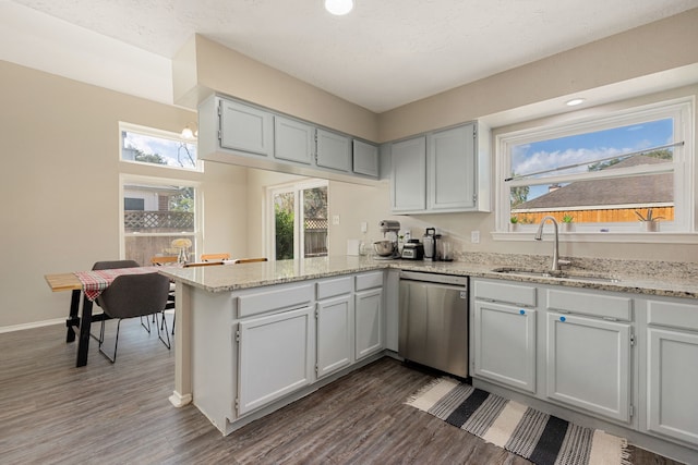 kitchen featuring light stone countertops, sink, dishwasher, kitchen peninsula, and dark hardwood / wood-style floors