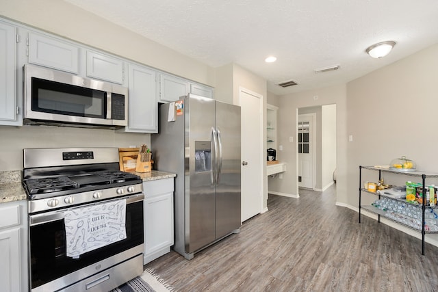 kitchen with appliances with stainless steel finishes, white cabinets, a textured ceiling, and light wood-type flooring