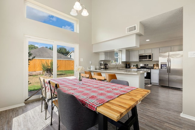 dining space with sink, a textured ceiling, a high ceiling, a notable chandelier, and dark hardwood / wood-style floors