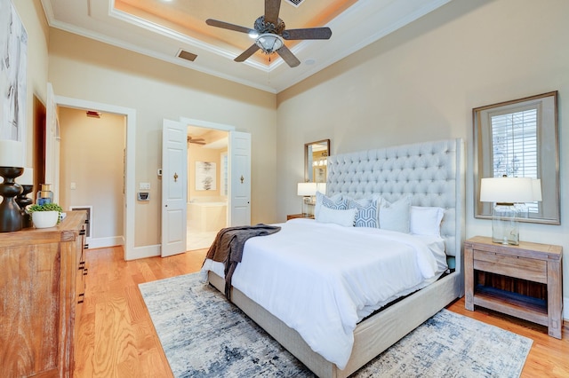 bedroom with light hardwood / wood-style floors, ceiling fan, a raised ceiling, crown molding, and ensuite bath