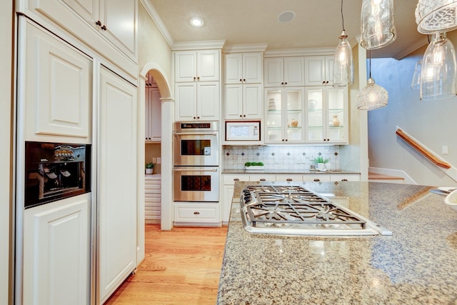 kitchen featuring light stone counters, appliances with stainless steel finishes, pendant lighting, light hardwood / wood-style floors, and white cabinets