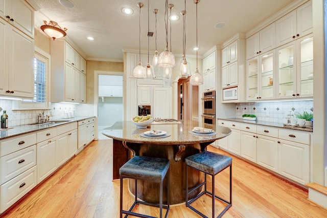 kitchen with backsplash, a sink, light wood finished floors, and white microwave