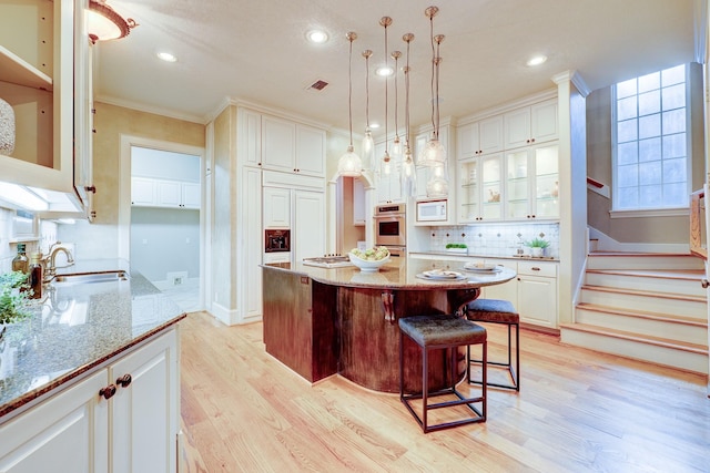 kitchen with light stone countertops, white microwave, a kitchen bar, a sink, and light wood finished floors