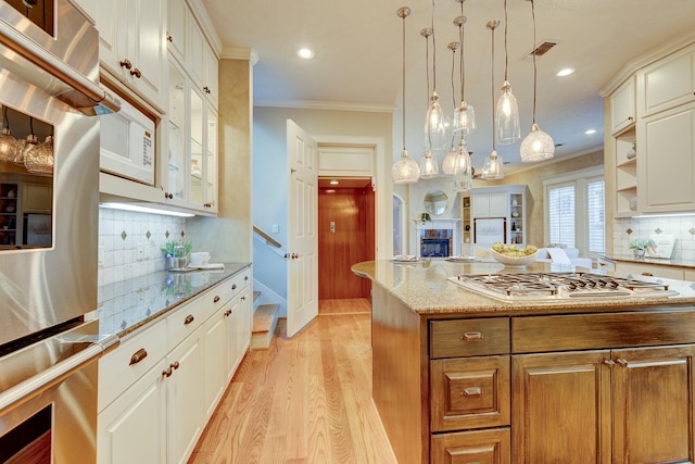 kitchen featuring light stone counters, hanging light fixtures, a kitchen island, stainless steel appliances, and white cabinets