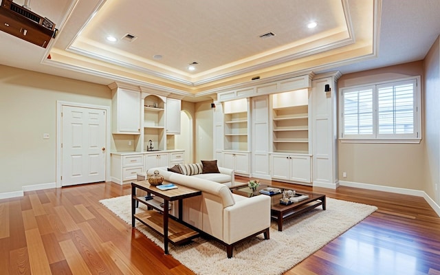 living area featuring light wood-style floors, baseboards, a tray ceiling, visible vents, and ornamental molding
