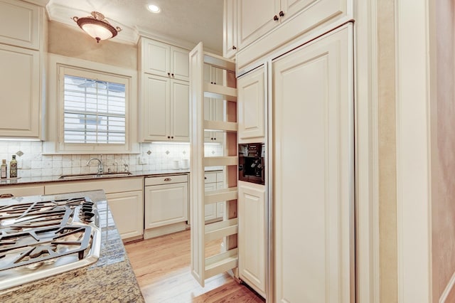 kitchen with stainless steel gas stovetop, sink, decorative backsplash, light hardwood / wood-style floors, and light stone countertops