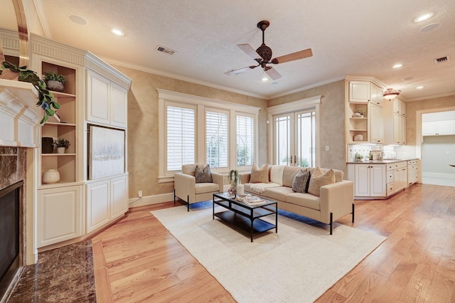 living room with crown molding, a high end fireplace, ceiling fan, and light hardwood / wood-style flooring