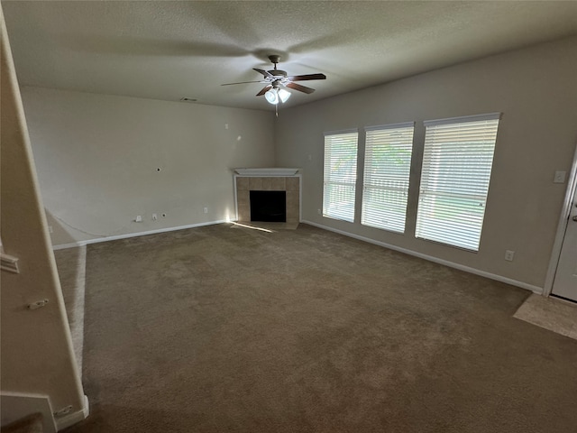 unfurnished living room with a tiled fireplace, a textured ceiling, dark carpet, and ceiling fan