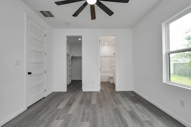 unfurnished bedroom featuring hardwood / wood-style floors, ensuite bathroom, ceiling fan, a closet, and a spacious closet