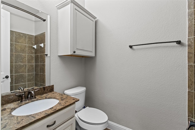 bathroom featuring a tile shower, vanity, and toilet