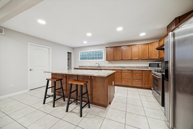 kitchen with light stone countertops, sink, stainless steel appliances, a breakfast bar, and a kitchen island