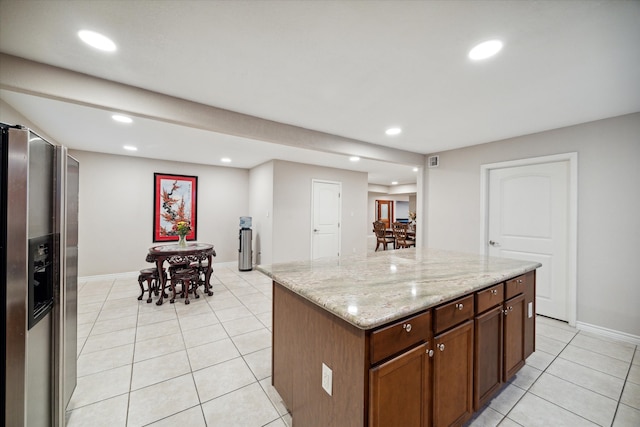 kitchen with a center island, stainless steel fridge, light stone counters, and light tile patterned floors