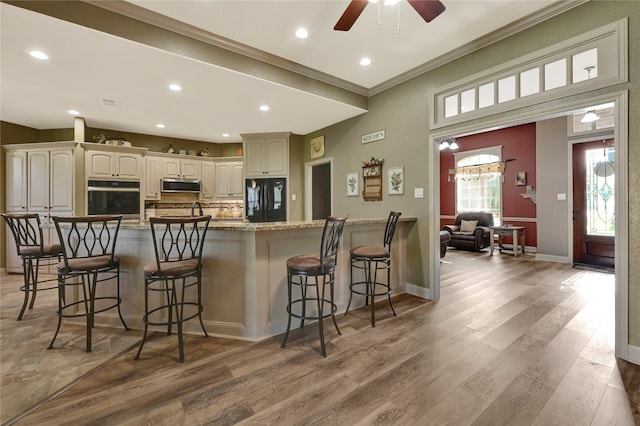 kitchen featuring appliances with stainless steel finishes, wood-type flooring, white cabinets, crown molding, and a breakfast bar