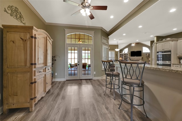 kitchen featuring french doors, light stone counters, crown molding, and light wood-type flooring