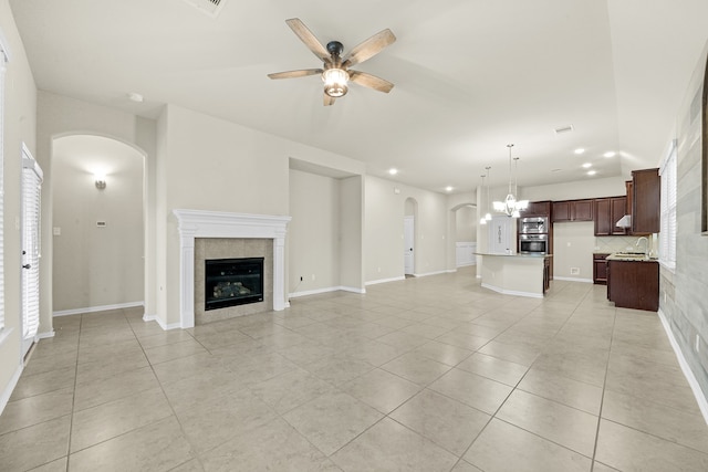 unfurnished living room featuring ceiling fan with notable chandelier, a fireplace, and light tile patterned floors