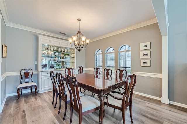 dining room with an inviting chandelier, ornamental molding, and light wood-type flooring