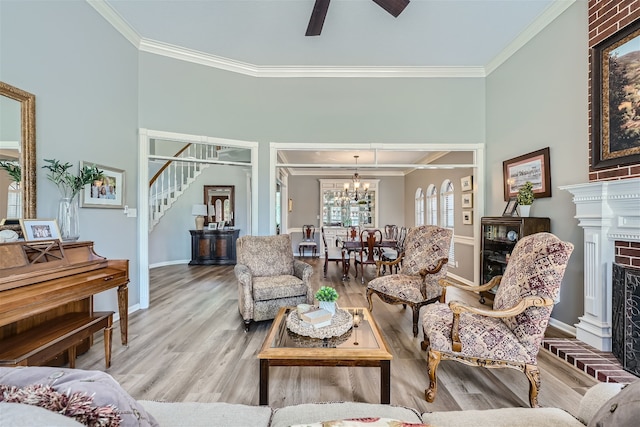 living room featuring wood-type flooring, ornamental molding, a brick fireplace, and ceiling fan with notable chandelier