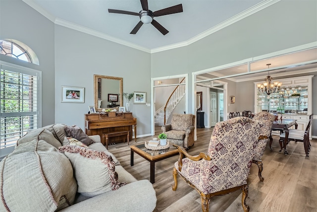 living room with a high ceiling, wood-type flooring, ornamental molding, and ceiling fan with notable chandelier